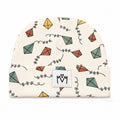 An off-white knit beanie hat featuring a repeating pattern of hand-drawn kites in muted green, orange, and yellow, connected by black squiggle lines. A white square patch on the folded cuff displays the black 'MM' logo.