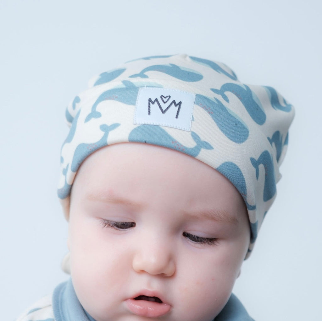 A beanie hat with a folded cuff, featuring a small white square patch on the front with a black embroidered logo.