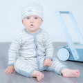 A baby sitting on a grey wooden floor wearing a light blue and white striped one-piece romper and matching beanie hat, with a light blue toy walker in the background.