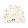 A cream-colored baby beanie hat with a colorful polka dot pattern in pink, yellow, green, and brown, featuring a white square patch on the folded cuff with a black embroidered 'M' logo.