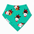 A triangular bandana-style bib in mint green with a repeating pattern of cartoon Santa Claus with musical instruments, featuring a white fabric tag on the left side that reads 'Millie and Me'.