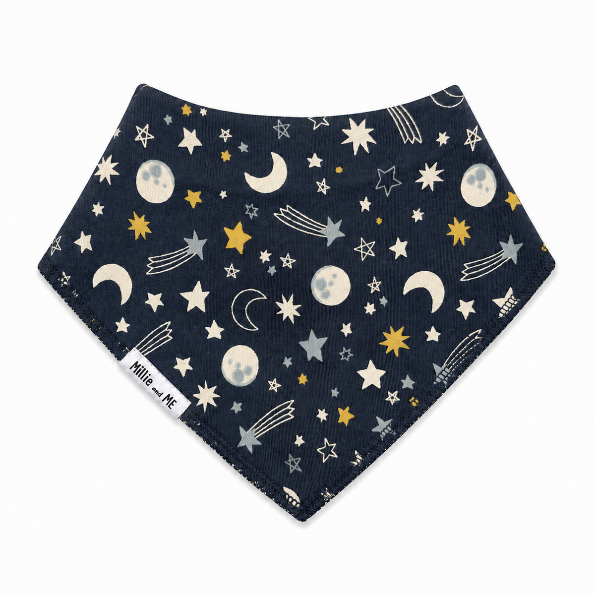 A triangular bandana bib with a dark navy blue space-themed print featuring stars, moons, and shooting stars, finished with a soft fleece border. A white fabric tag on the left side reads 'Millie and Me'.