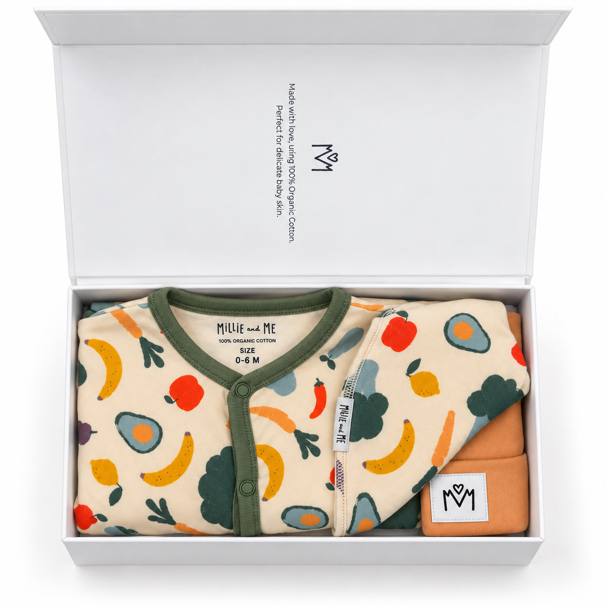 A folded baby outfit set inside an open white gift box. The set includes a cream-coloured cotton babygrow with a colourful fruit and vegetable print and olive green trim, and a matching folded piece in warm peach with a white logo patch.